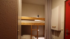 Una cama individual superpuesta con escalera, una puerta blanca y una pared roja.