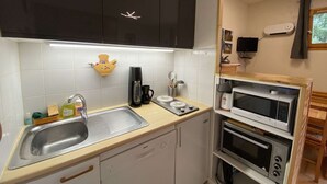 Cocina compacta con lavamanos, cafetera y electrodomésticos apilados, incluyendo microondas y horno.