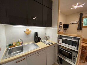 Una cucina compatta con lavandino, macchina del caffè ed elettrodomestici impilati, tra cui forno a microonde e forno.