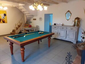 Une table de billard dans une pièce avec un escalier, une armoire blanche et un miroir au mur.