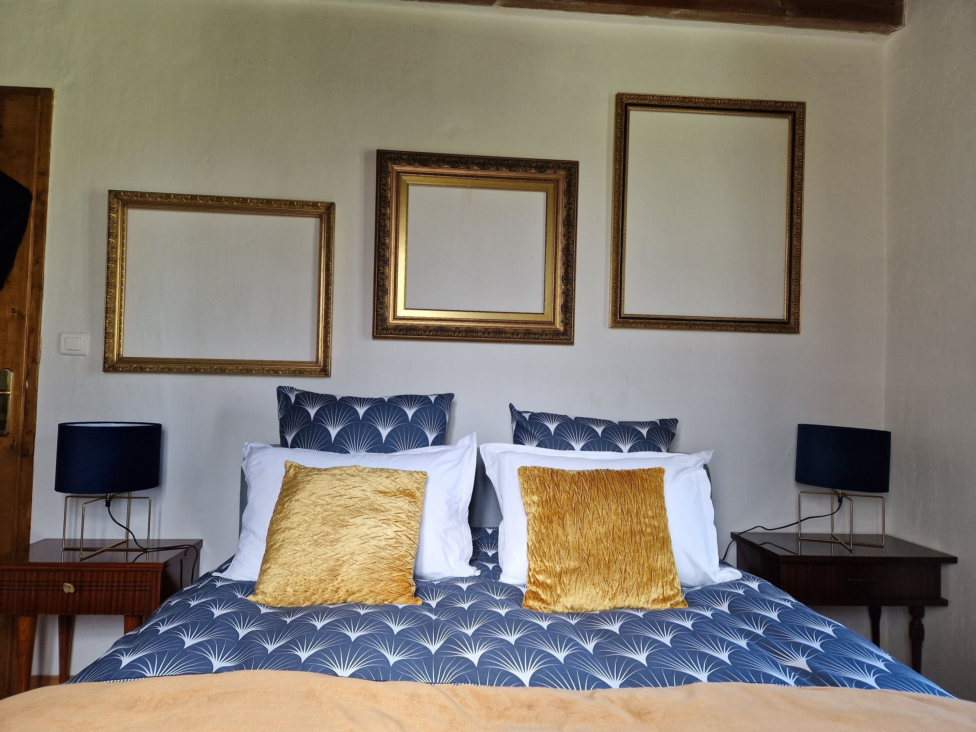 A bedroom with a bed, two nightstands, and three framed mirrors on the wall.