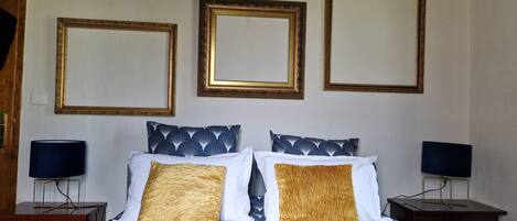 Un dormitorio con una cama, dos mesitas de noche y tres espejos enmarcados en la pared.