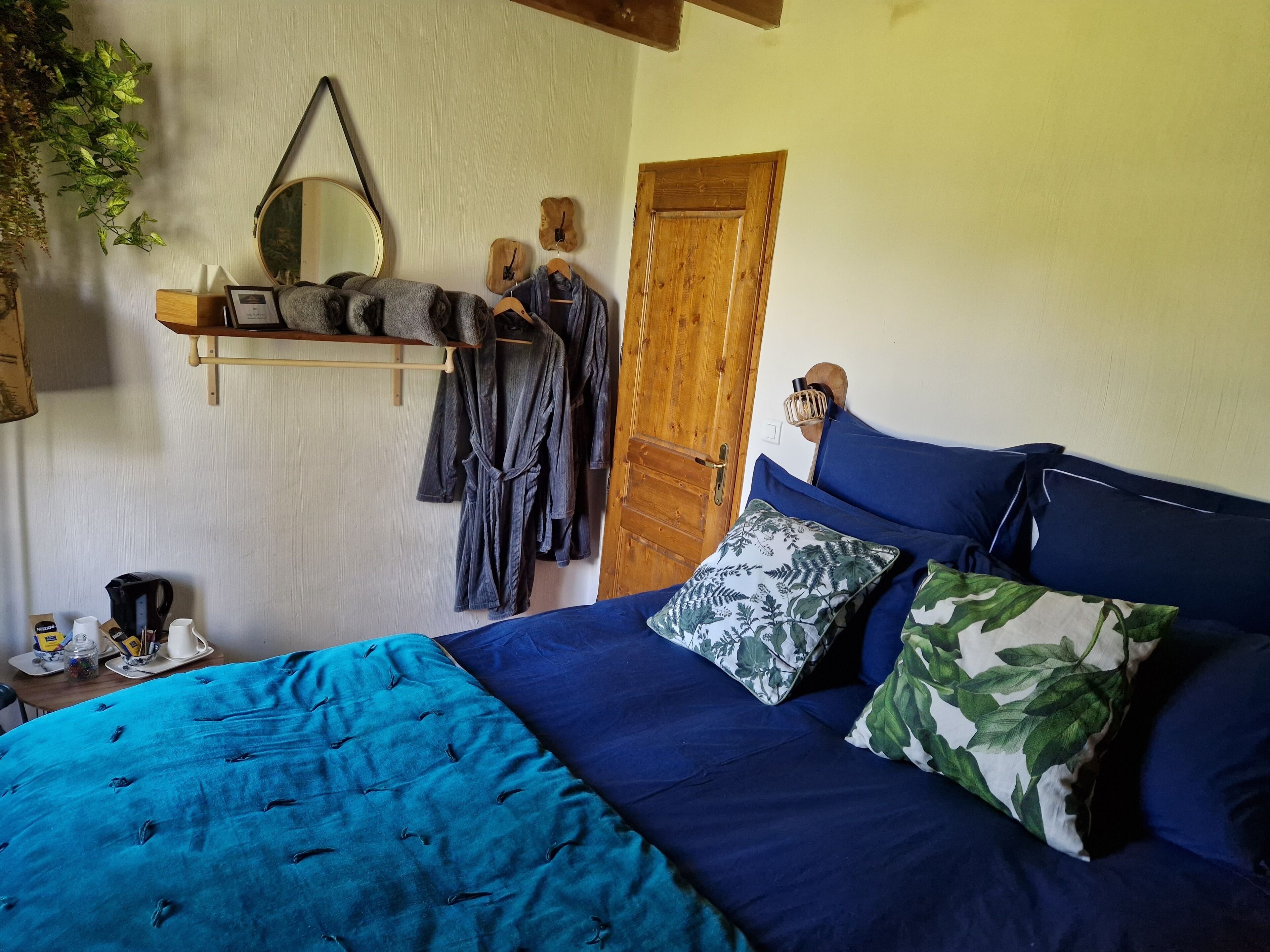 Un dormitorio con una cama grande, una puerta de madera, un espejo y una estantería con ropa y una cafetera.