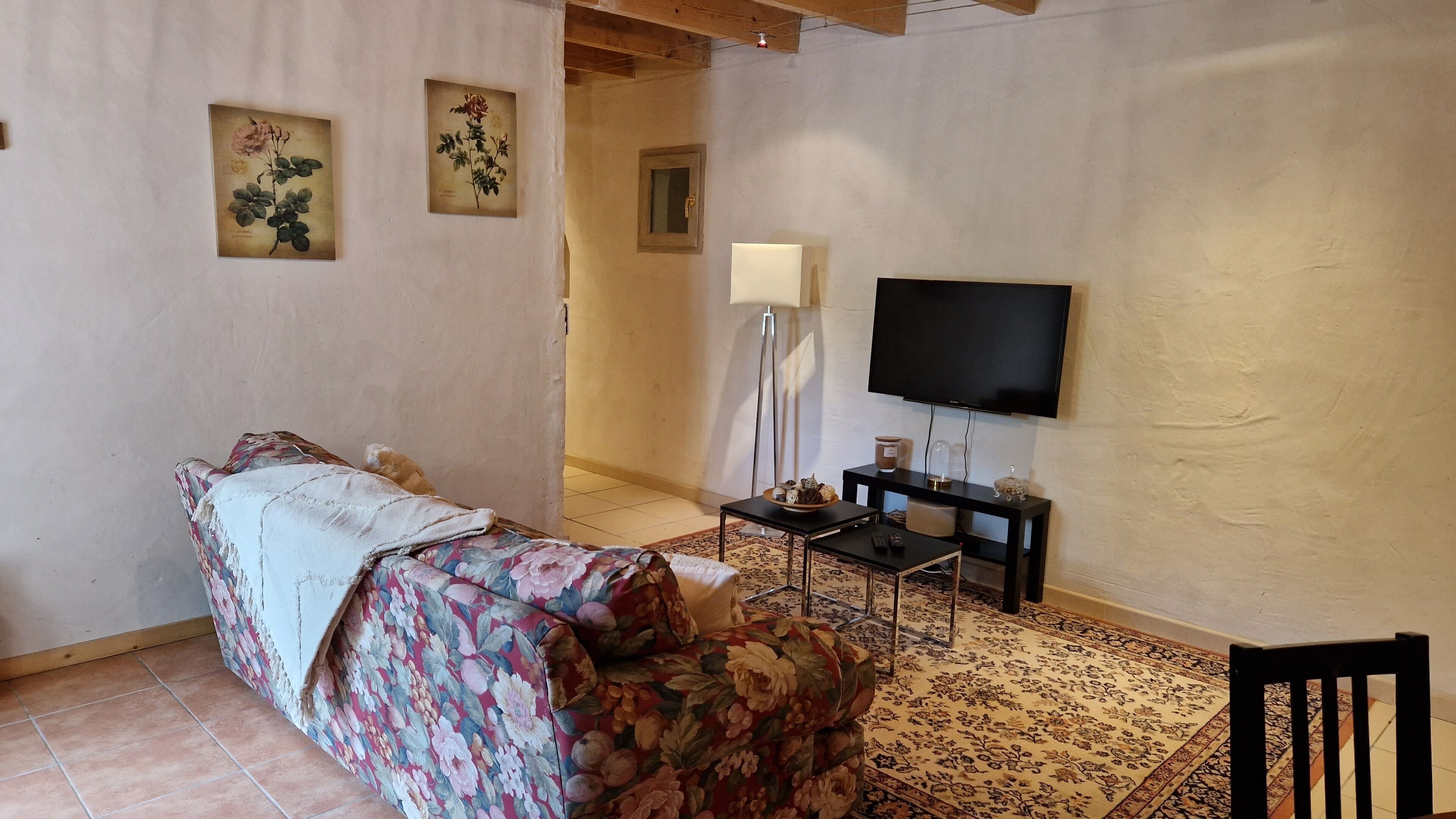 A cozy room with a bed, a TV, a small table with a lamp, and a chair.