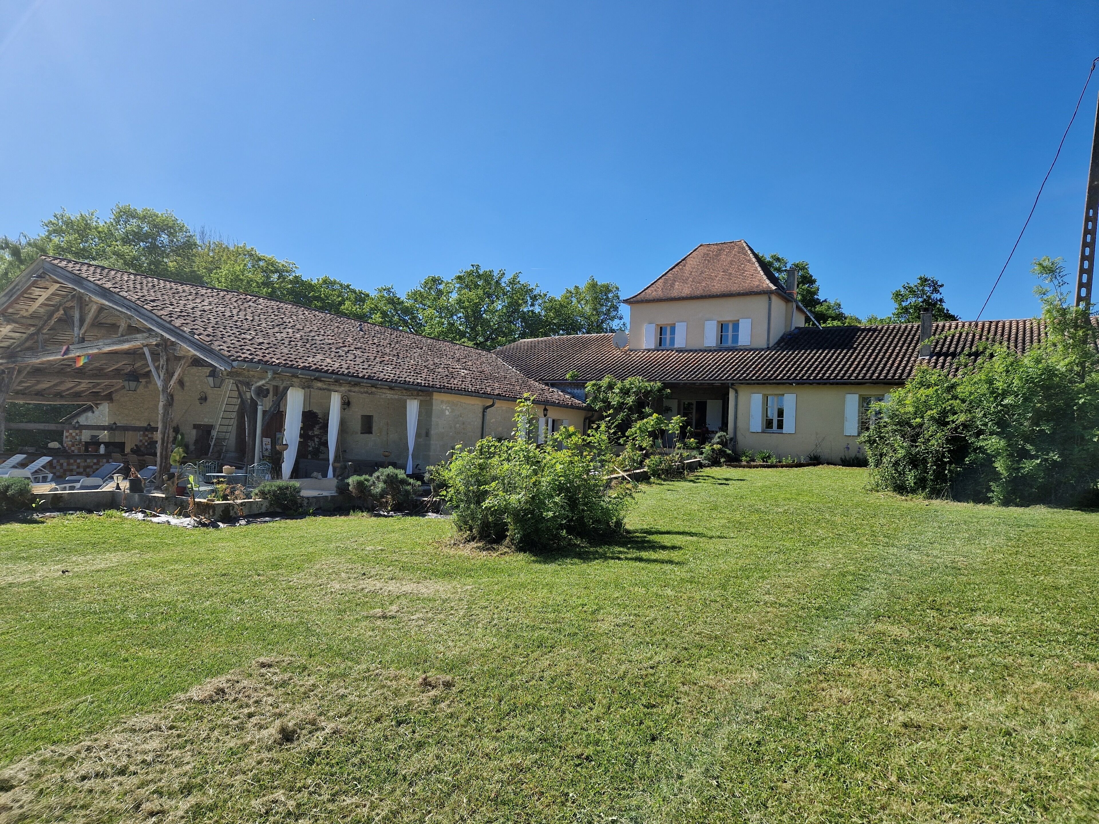 A two-story house with a tiled roof, a covered patio area, and a well-maintained lawn.