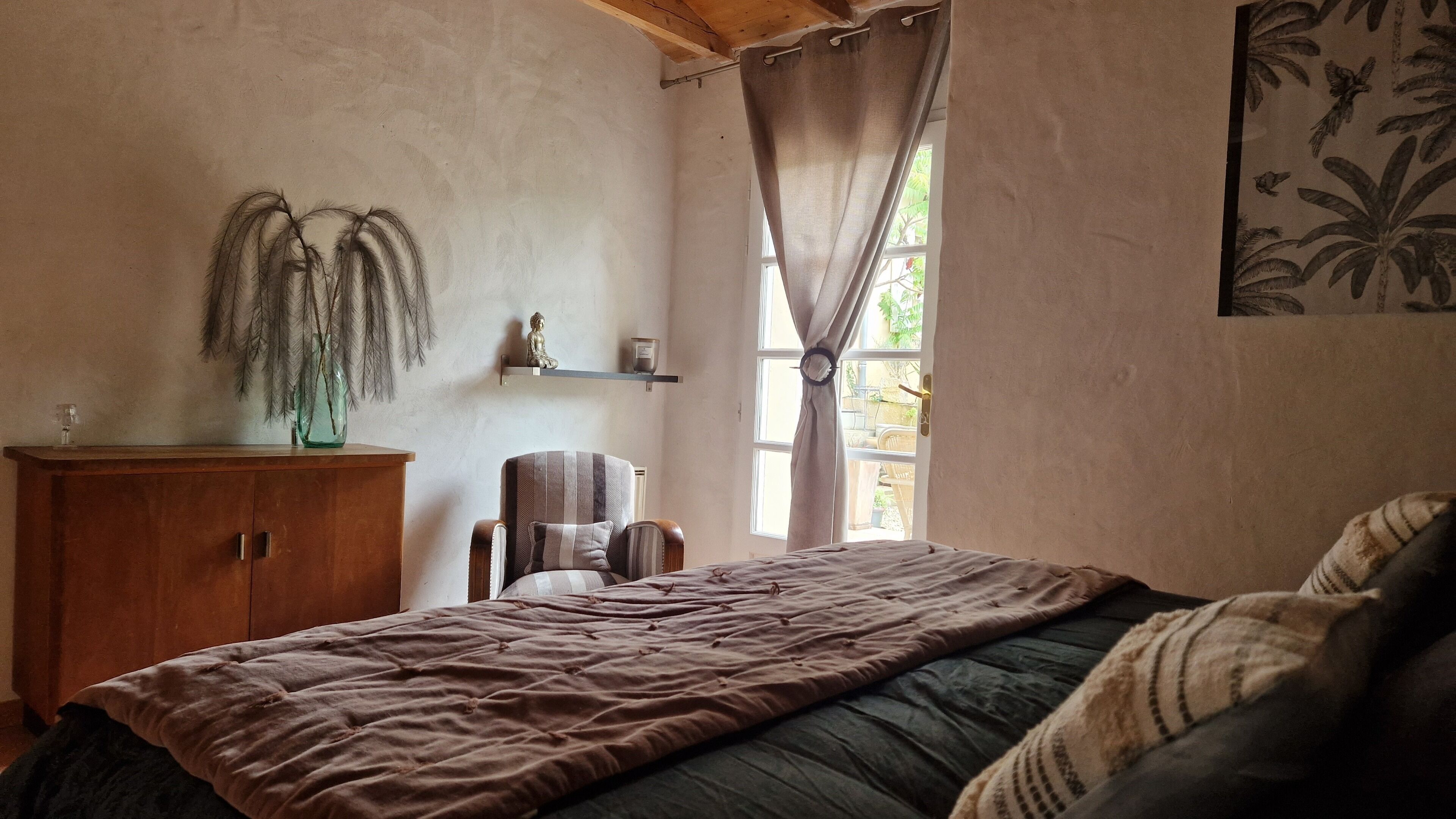 A bedroom with a bed, a wooden cabinet, a chair, a shelf with a statue, and a window with curtains.