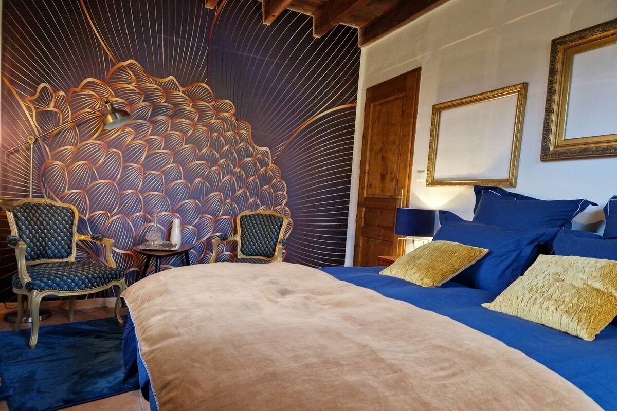A bedroom with a large bed, two chairs, a small table, and a decorative wall.
