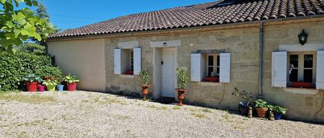 A stone building with a tiled roof, a gravel driveway, and potted plants.