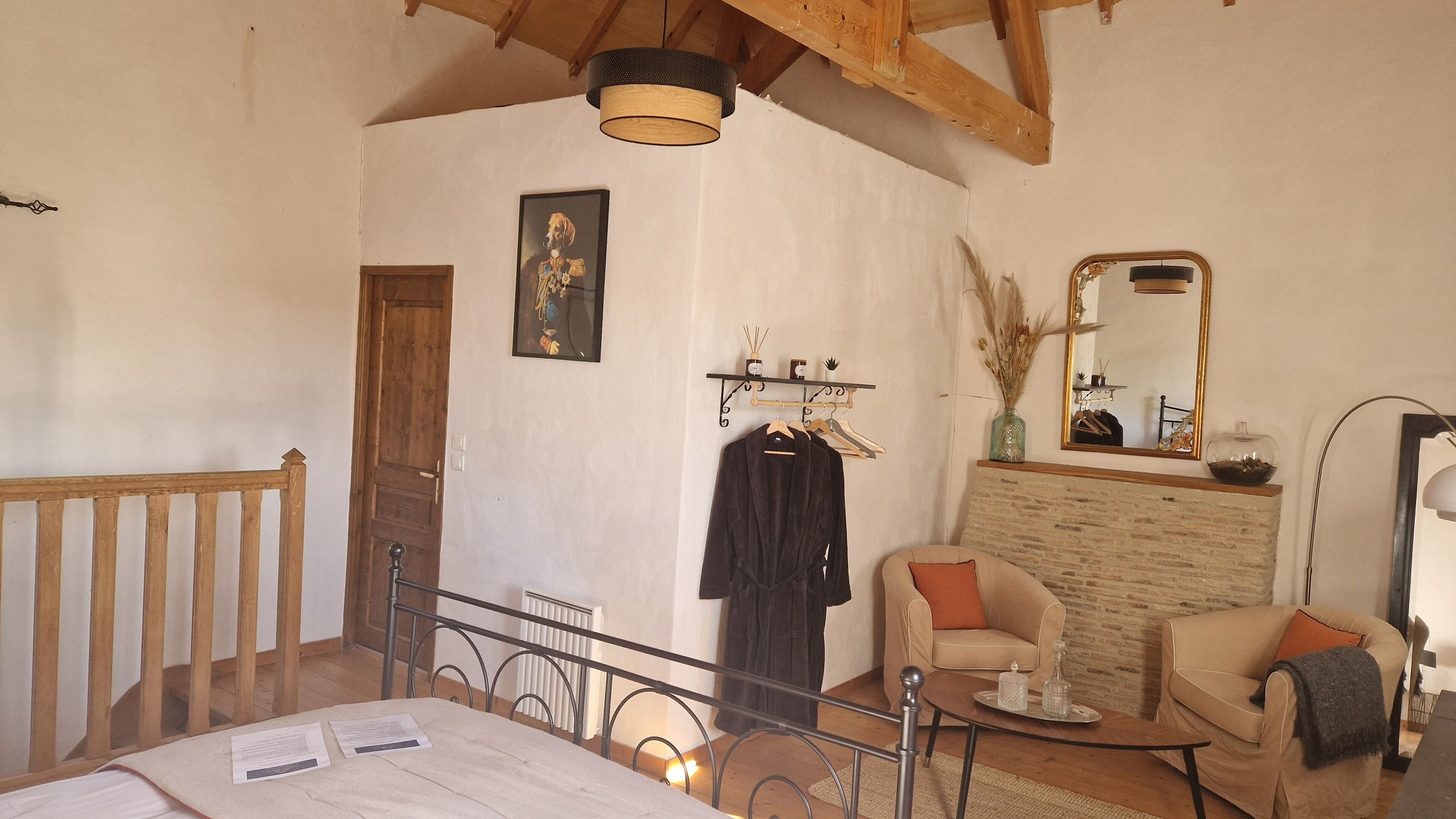 Un dormitorio con techo de madera, una cama con papeles encima, una silla, una mesita con una bandeja y un espejo en la pared.