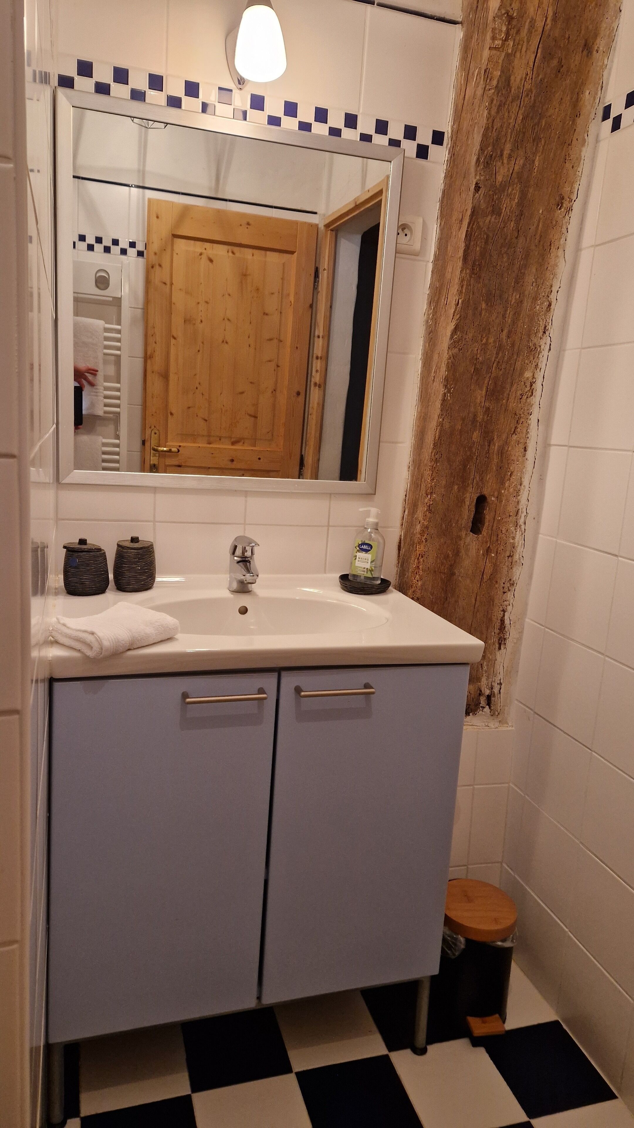 A bathroom with a white sink, a mirror, and a wooden door. There is a bottle of hand soap on the sink.