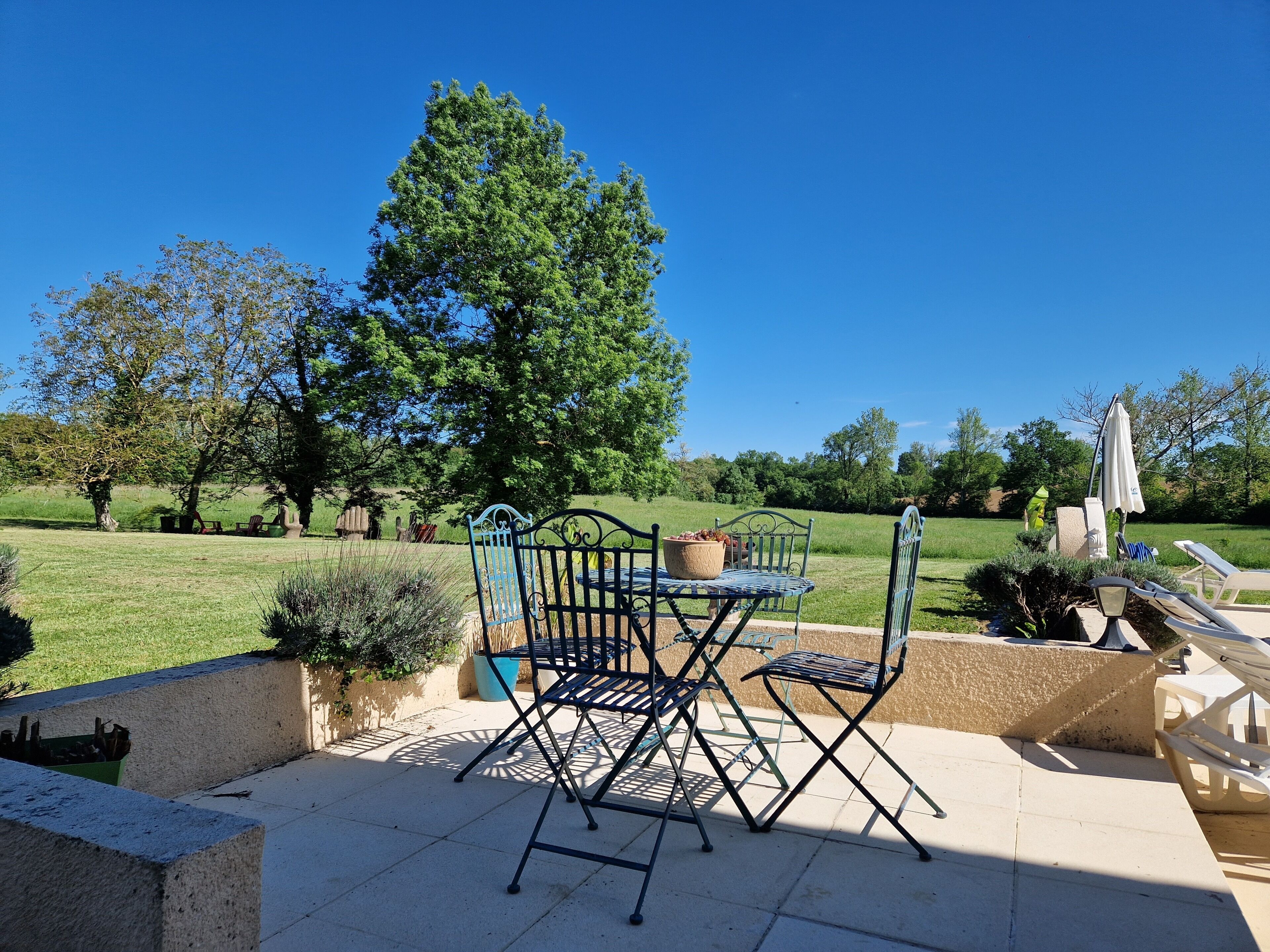 An outdoor patio with a table and chairs, surrounded by greenery and trees.
