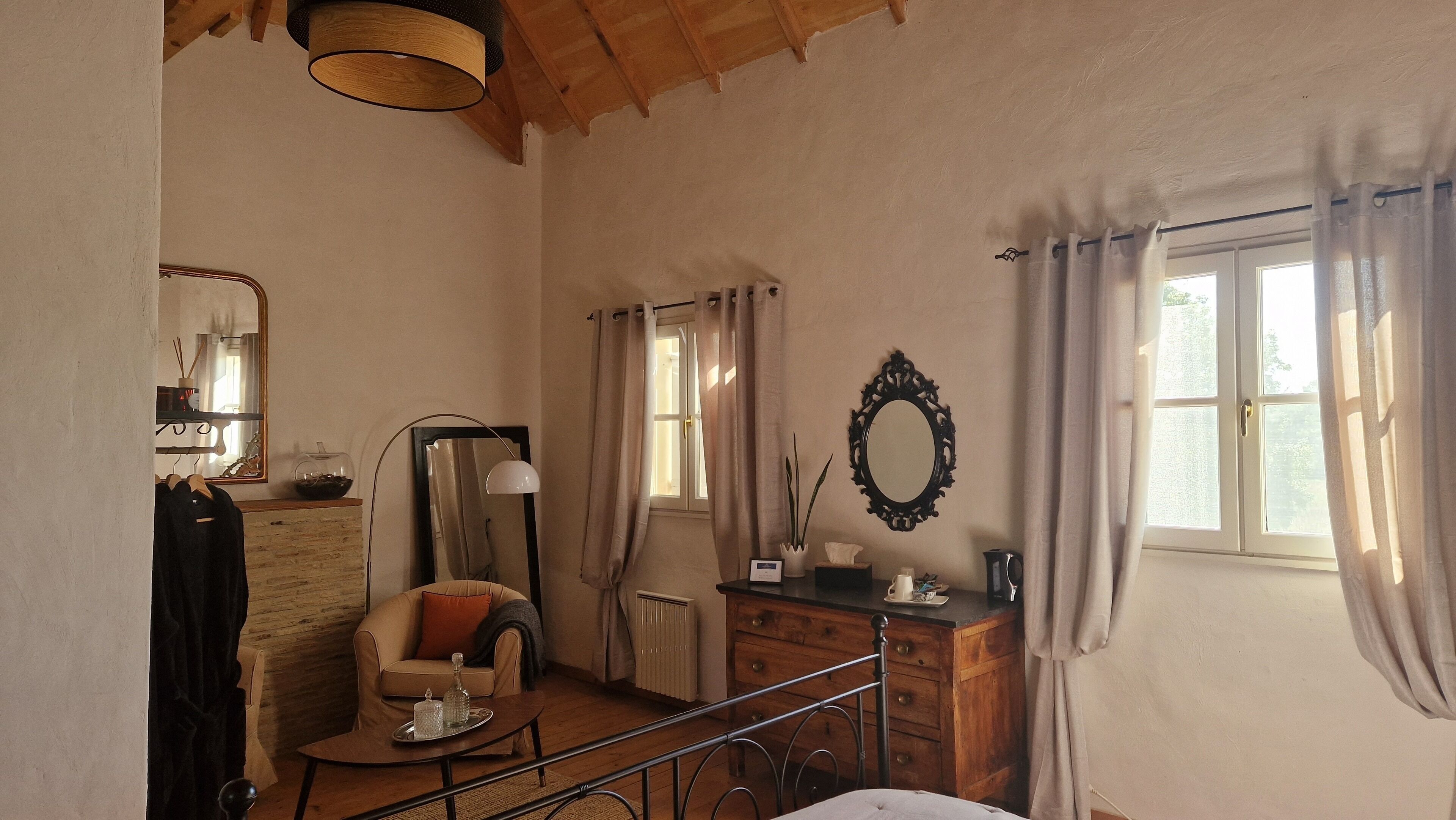 Una habitación acogedora con techo de madera, un sofá, una mesita con una bandeja, un aparador, un espejo y una ventana con cortinas.