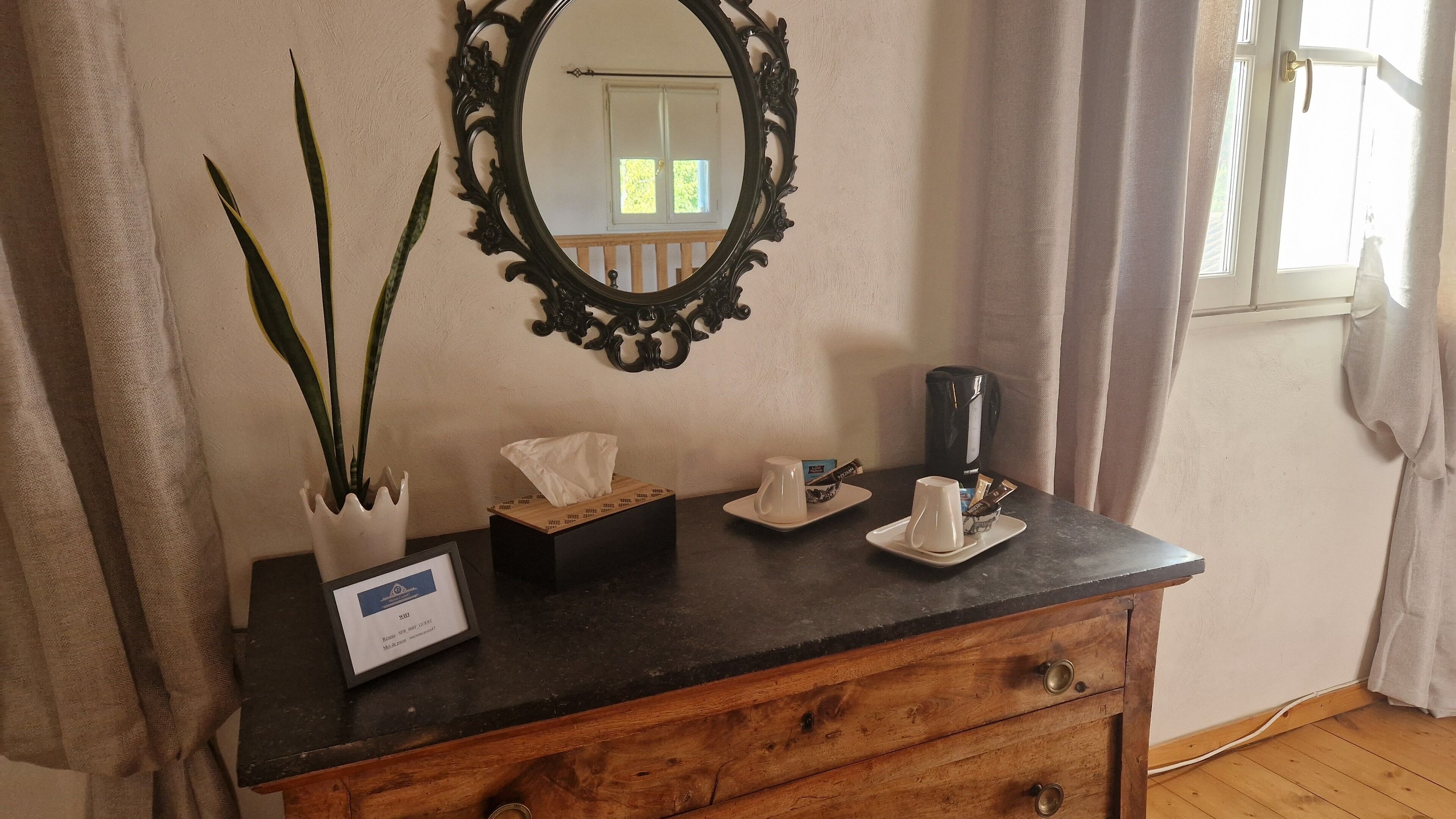 Ein hölzerner Nachttisch mit Spiegel, Taschentuchbox, Kaffeemaschine und Tasse.