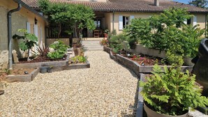Uma casa com telhado telhado, um jardim com diversas plantas e um caminho de brita que leva à entrada.