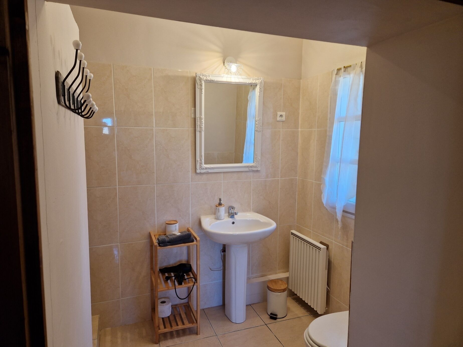 A bathroom with a sink, mirror, and toilet. There is a towel rack and a small shelf with toiletries.