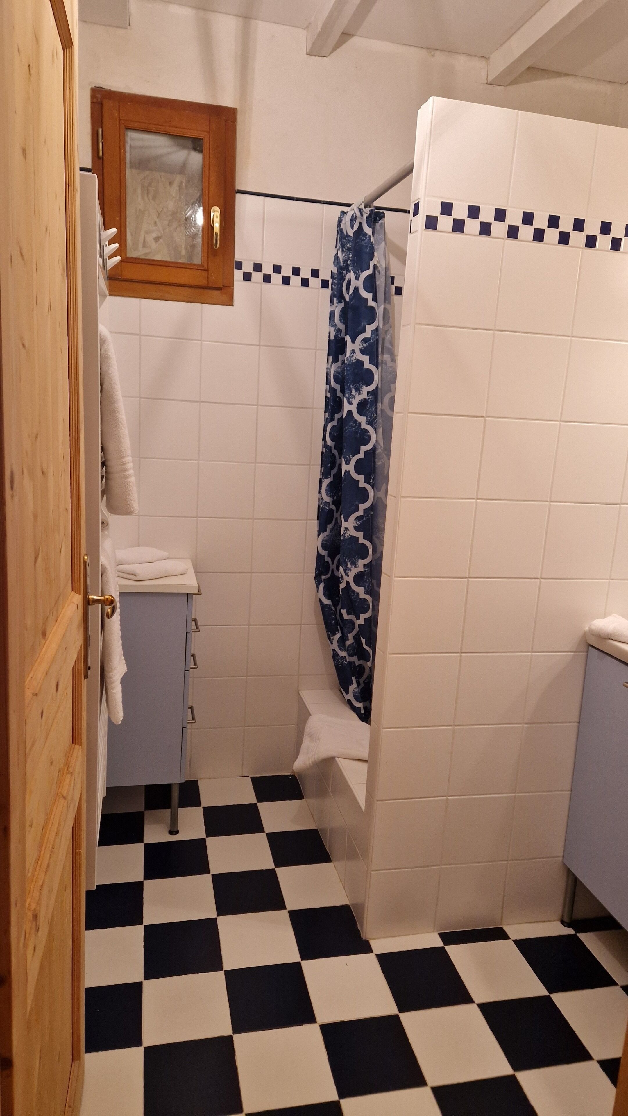 Une salle de bain avec un carrelage à motifs géométriques, des toilettes blanches, un rideau de douche bleu et une porte en bois.