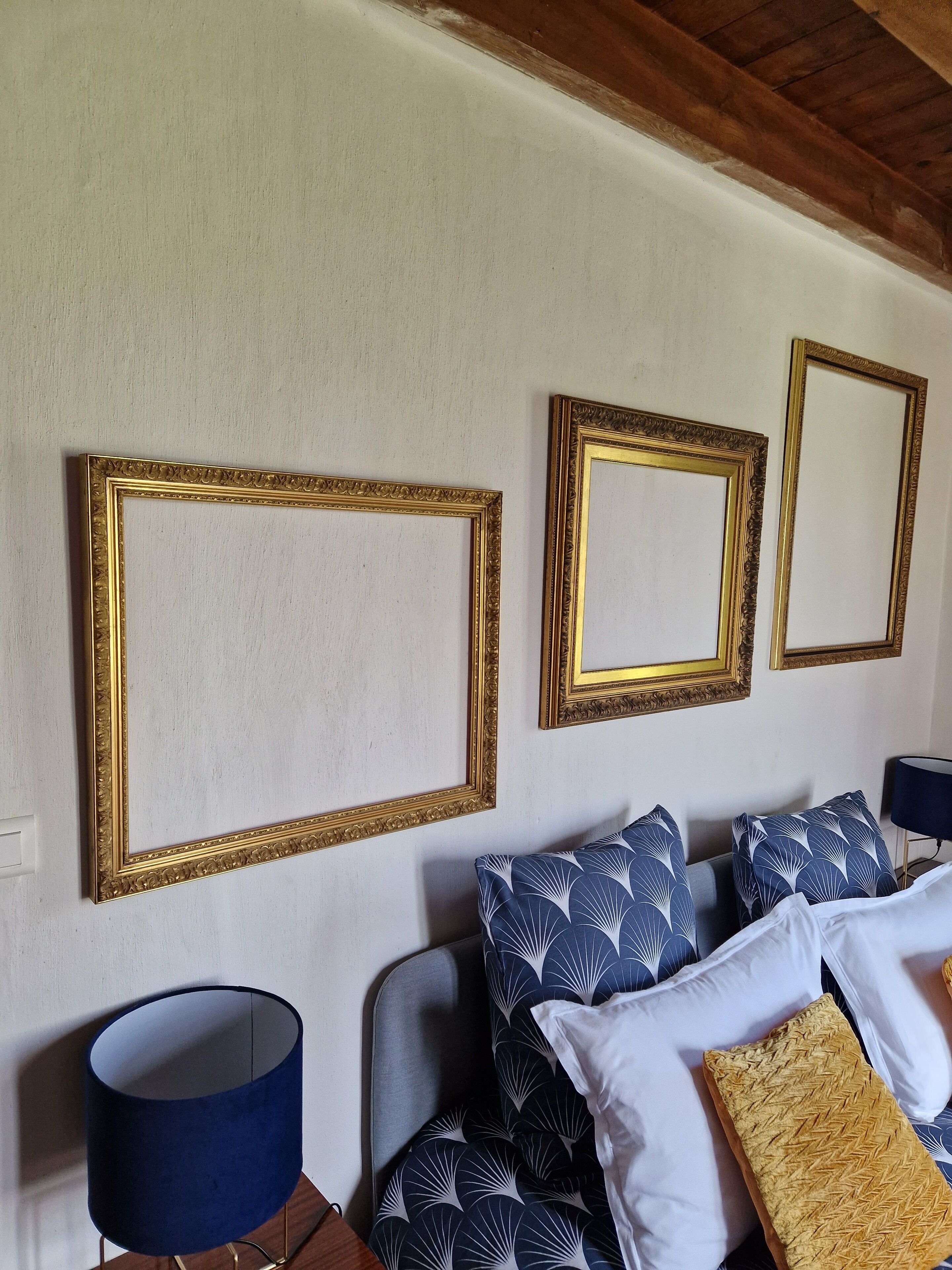 A room with a bed, pillows, a lamp, and three wall-mounted picture frames.