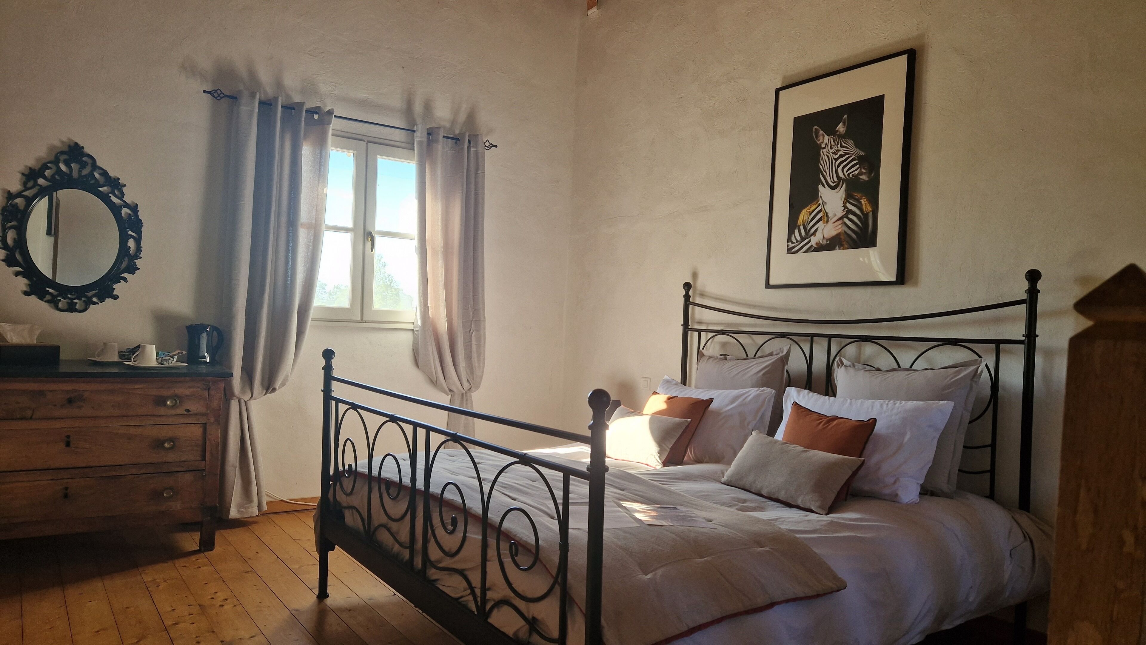 Une chambre à coucher avec un lit à baldaquin, une commode en bois, un miroir et une fenêtre avec des rideaux.