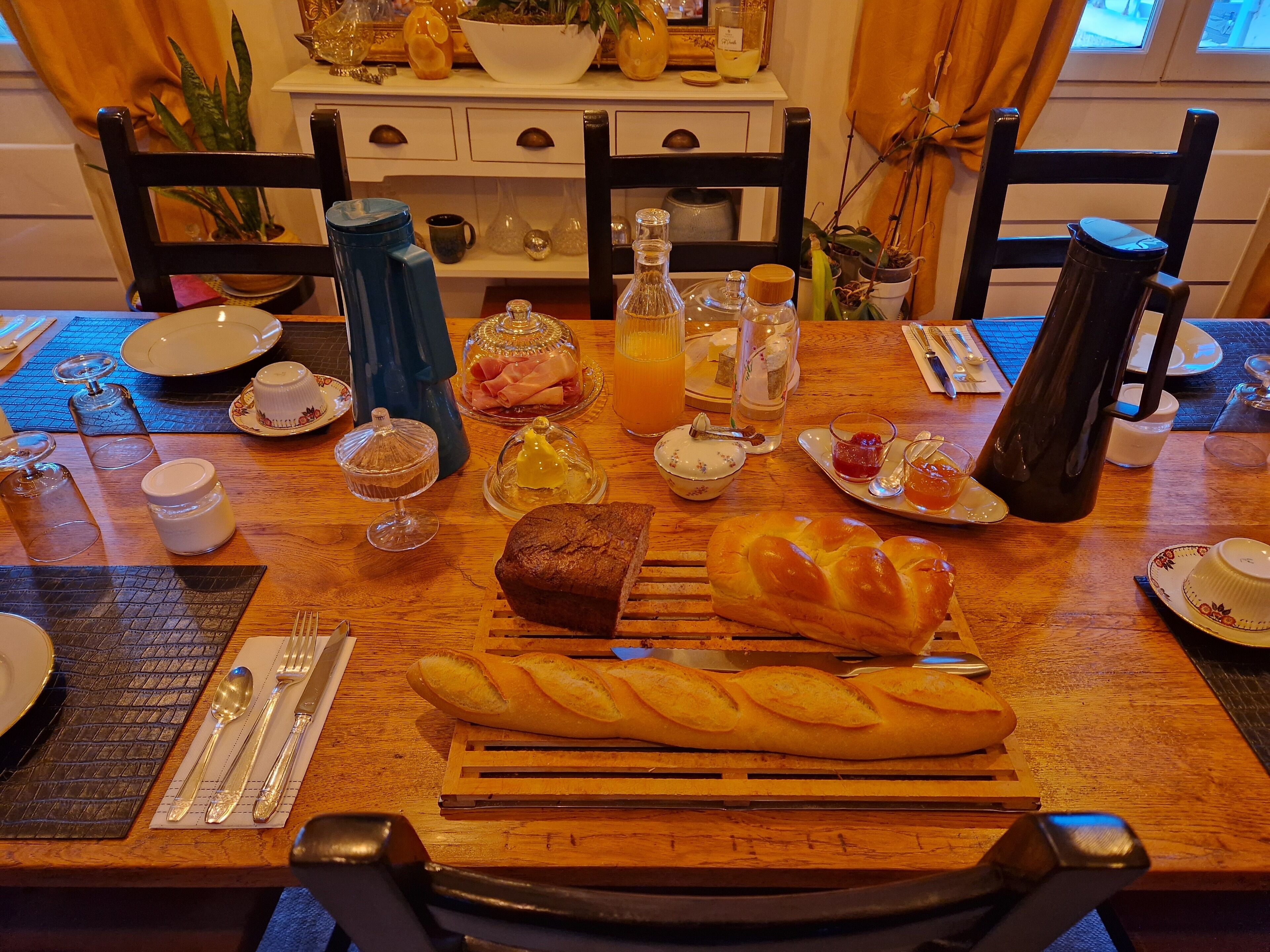 Une table de petit-déjeuner avec du pain, du beurre, de la confiture et une cafetière.