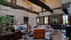 Uma sala de estar espaçosa com pé direito alto, vigas de madeira aparente, um candelabro e um espaço de jantar com mesa e cadeiras.