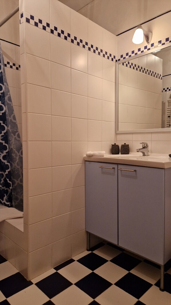 Un baño con azulejos blancos, piso a cuadros blancos y negros, un lavamanos y un espejo.