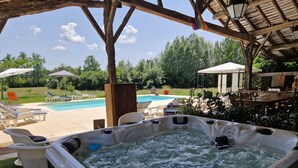 Ofurô com pergolado de madeira, piscina e área de estar ao ar livre.