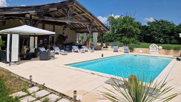Área de piscina com espreguiçadeiras, um espaço de estar coberto e uma parede de pedra.