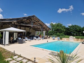 Un área de piscina con sillones de descanso, una zona de estar techada y un muro de piedra.