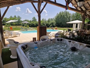 A hot tub with a wooden pergola overhead, a pool, and outdoor seating.