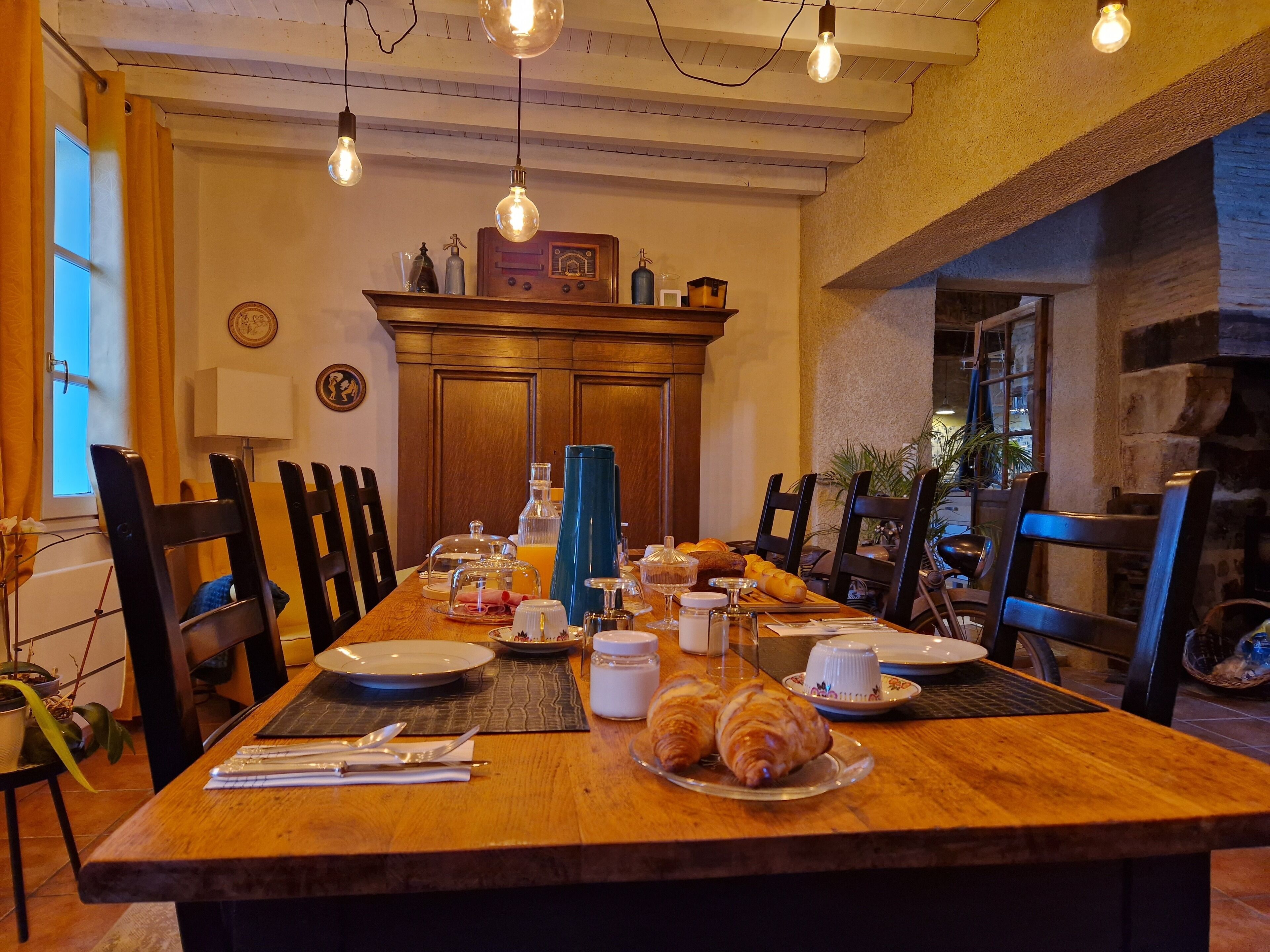 A dining area with a wooden table set for breakfast, including croissants and orange juice.