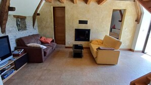 A spacious living area with a high ceiling and exposed wooden beams. There is a television mounted on the wall, a sofa, and a coffee table. - La Bergerie, oasis of calm for visiting the LOT and the Dordogne (Montgesty)