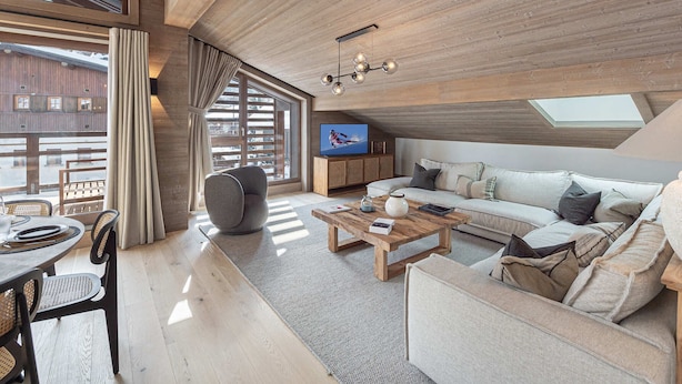 Una sala de estar moderna con techo de madera, ventanas grandes, televisor, sofá y zona de comedor.