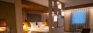Une chambre moderne avec un plafond en bois, un lit avec une literie blanche, une table de chevet, une chaise et une grande fenêtre avec des rideaux.