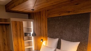 Quarto com paredes de madeira, cama com roupa branca e estante com telefone e livros.