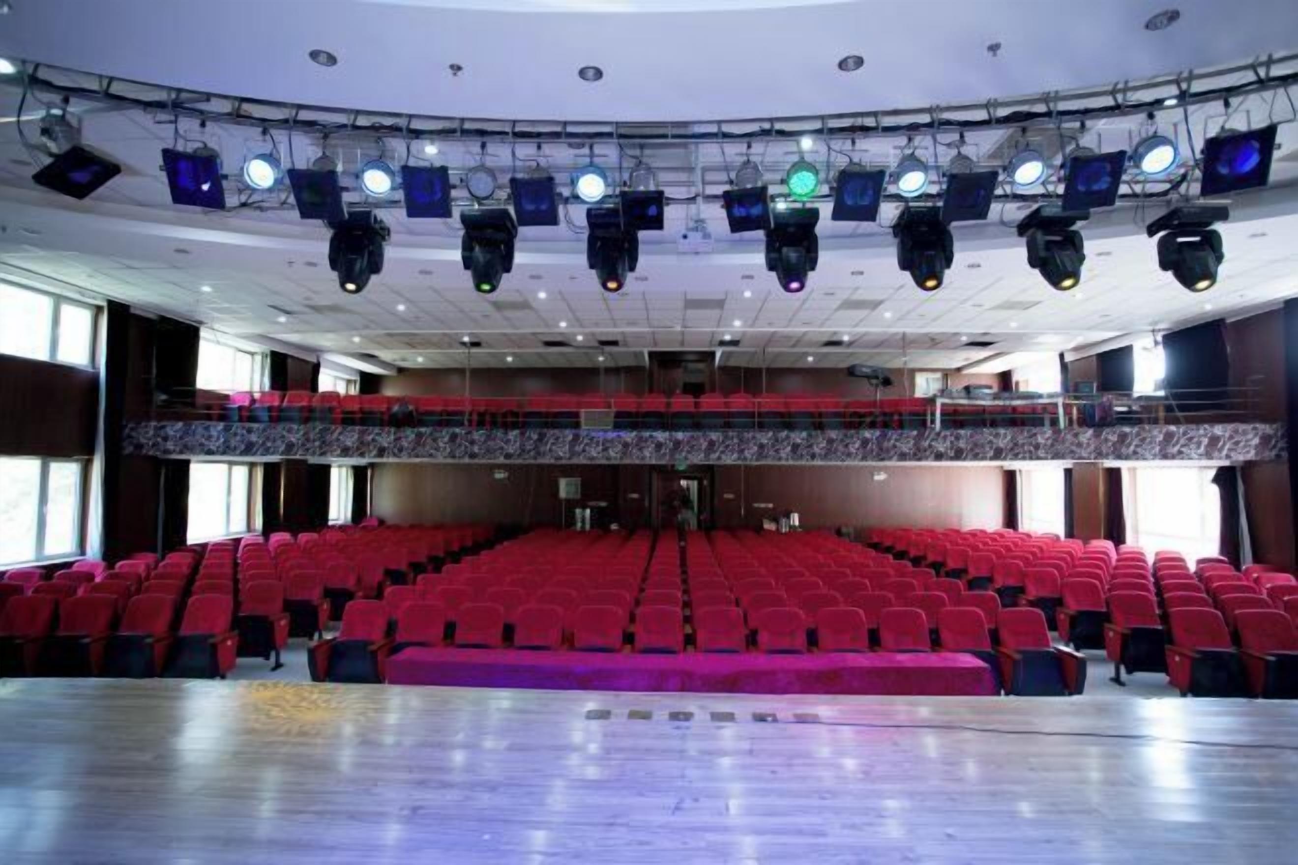 Een grote zaal met rijen rode stoelen, een podium met lichtinstallatie, en een balkon.