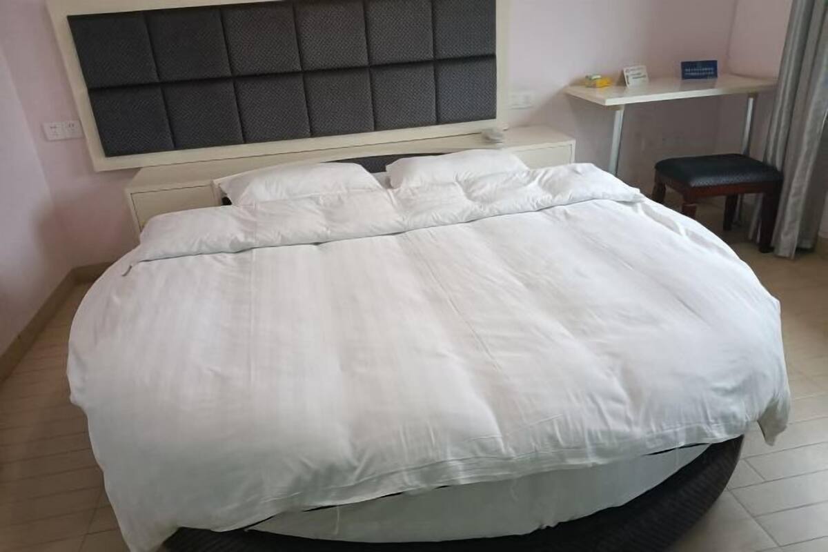 Una cama bien hecha con cabecera, un pequeño escritorio con silla y una ventana con cortinas.