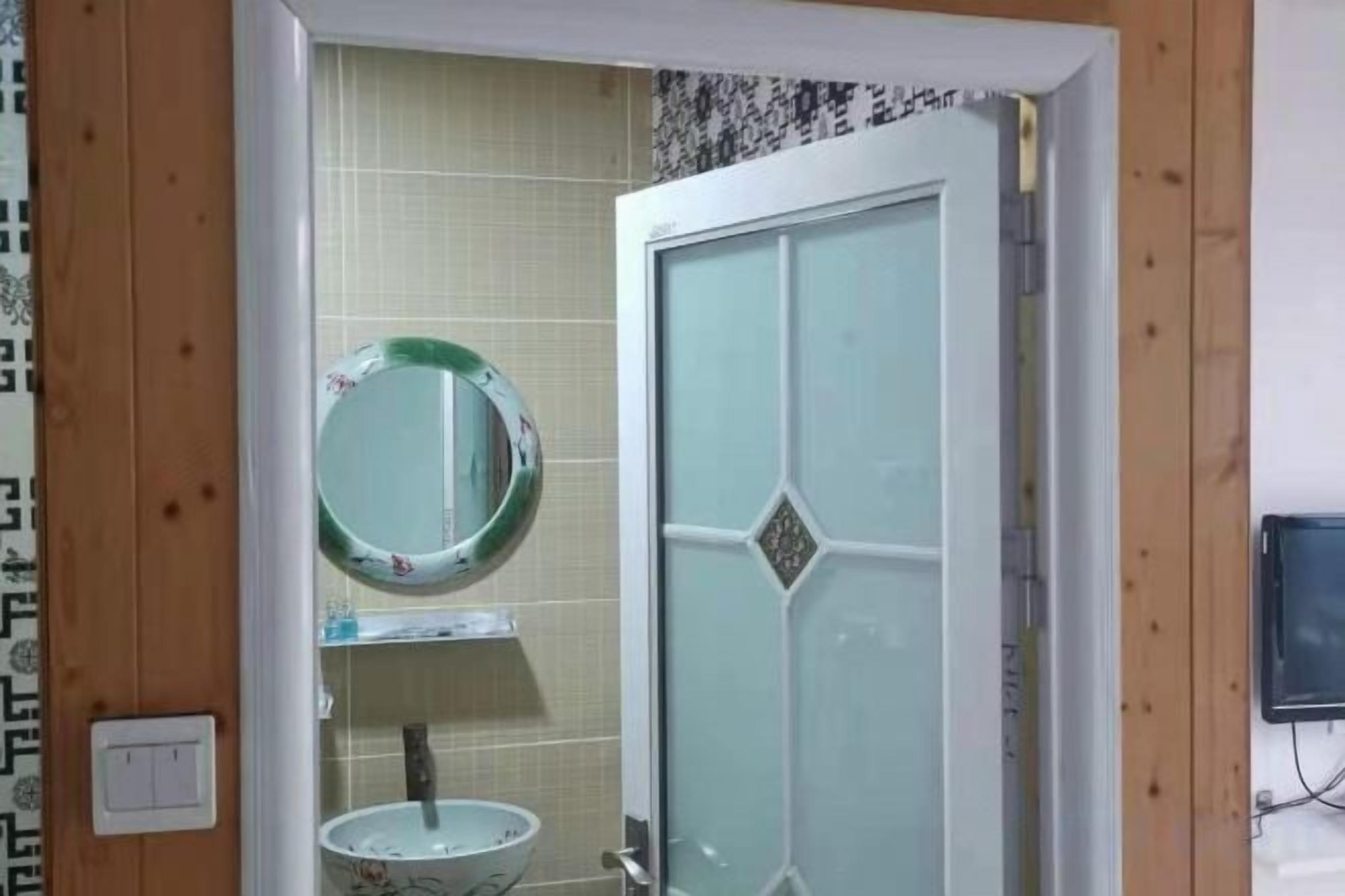 Un baño con puerta de cristal, un espejo redondo y un lavabo blanco.