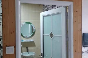 A bathroom with a glass door, a round mirror, and a white sink.