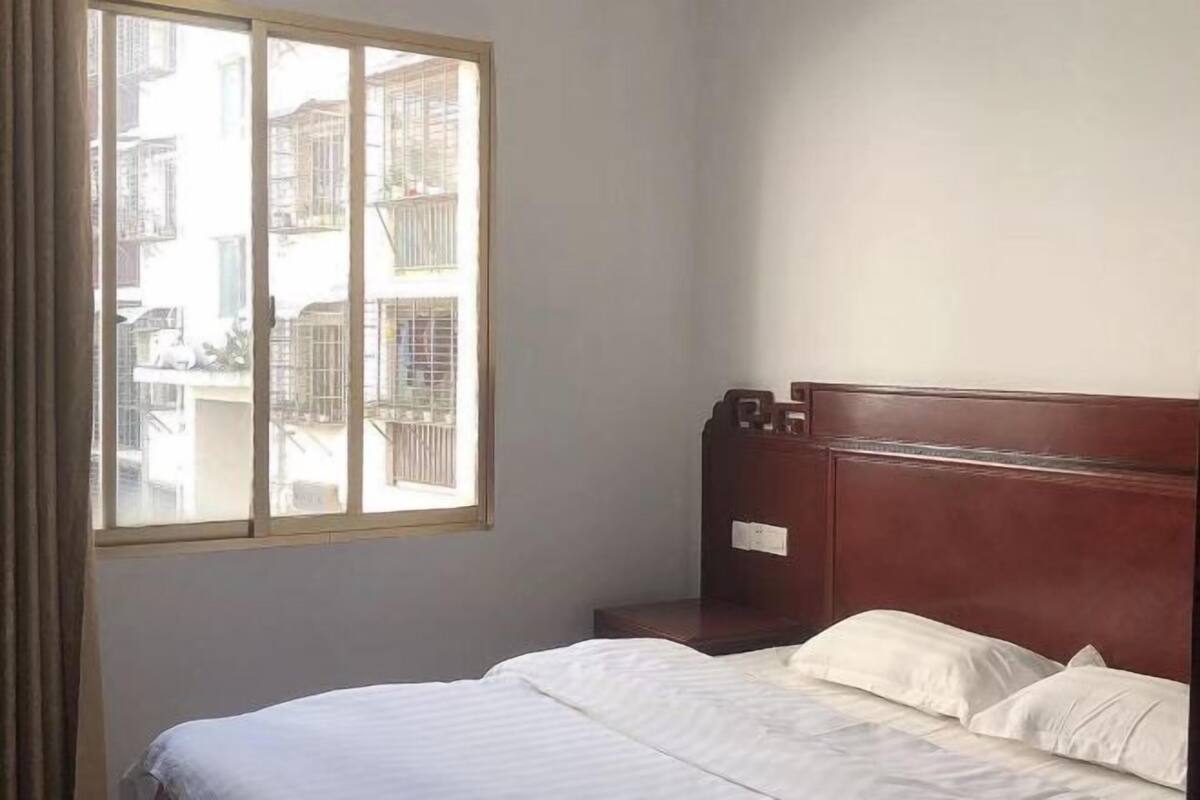 Habitación de hotel con cama, mesita de noche y ventana con vistas a edificios.