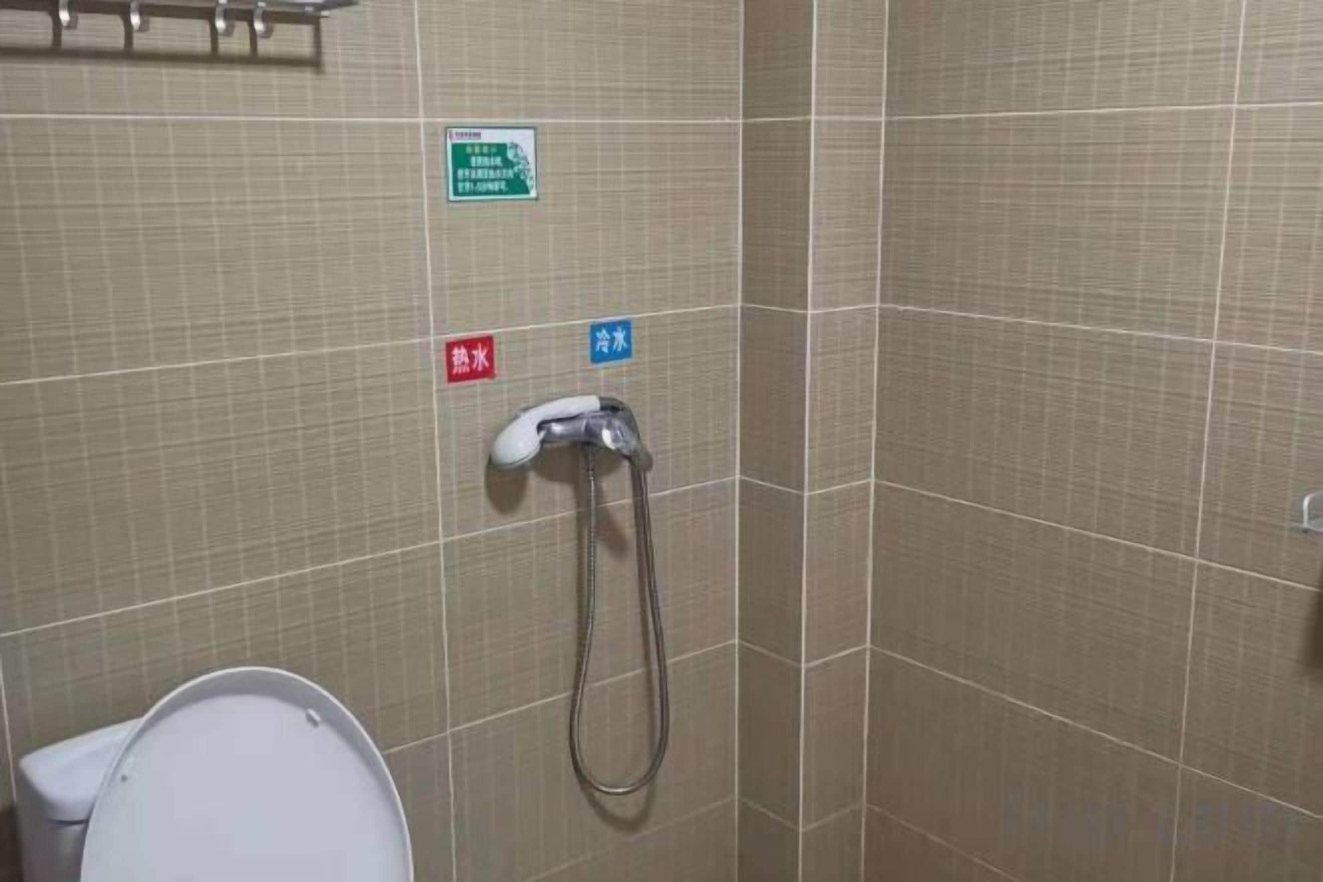 A bathroom with a toilet, a shower, and two signs indicating hot and cold water.