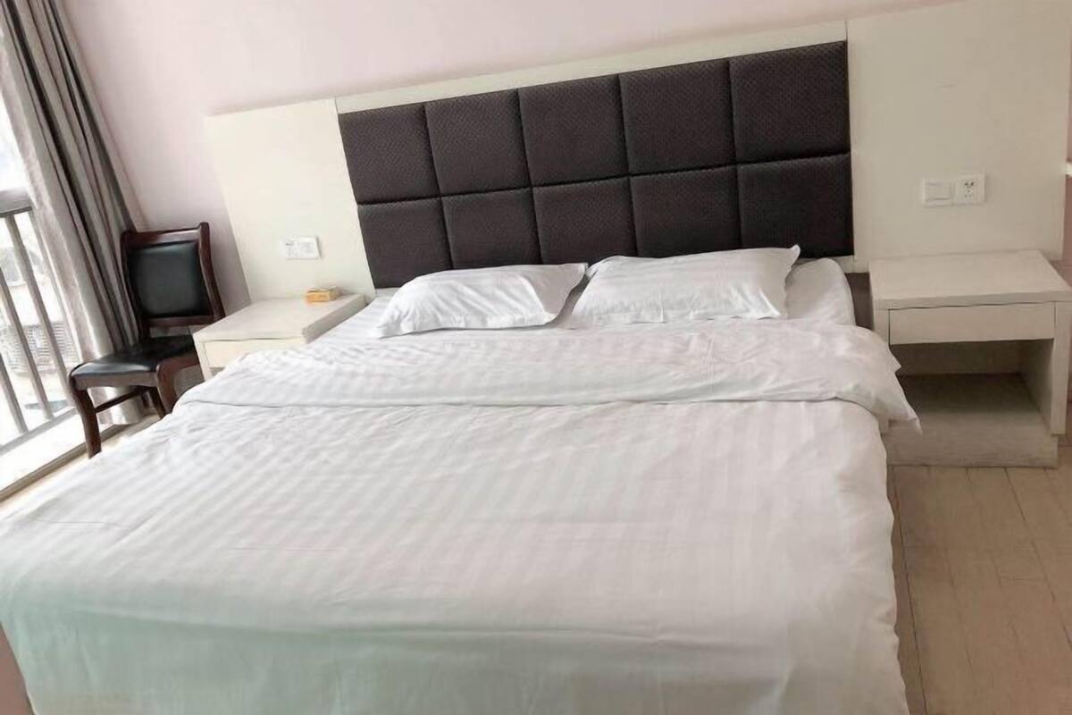 Una cama bien tendida con sábanas blancas, cabecera acolchada oscura y una mesita de noche con lámpara.