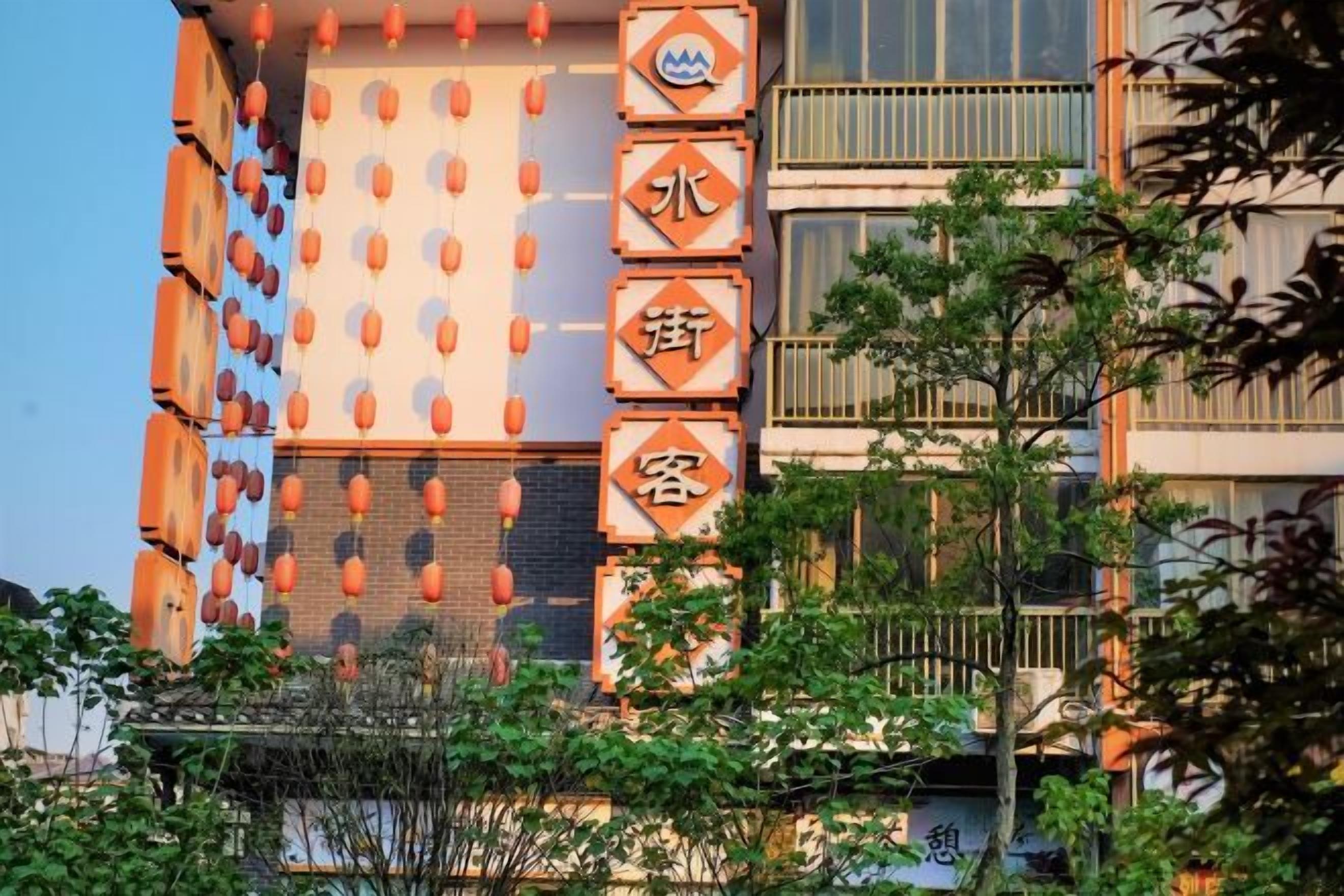 Un immeuble à plusieurs étages, doté d’une enseigne verticale ornée de caractères chinois, de balcons et surplombant un ciel dégagé.