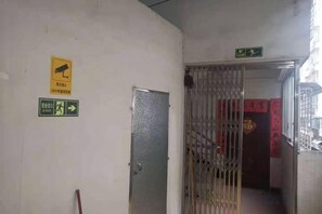 A corridor with a security camera sign, an exit sign, and a metal door. - Shui Jie Hostel (Xing'an County)