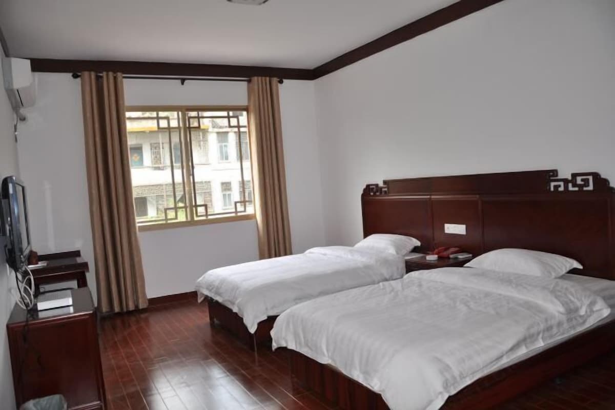 A hotel room with two single beds, a wooden headboard, a desk with a chair, and a window with curtains.