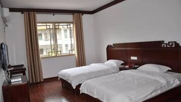 Habitación de hotel con dos camas individuales, un cabecero de madera, un escritorio con una silla y una ventana con cortinas.