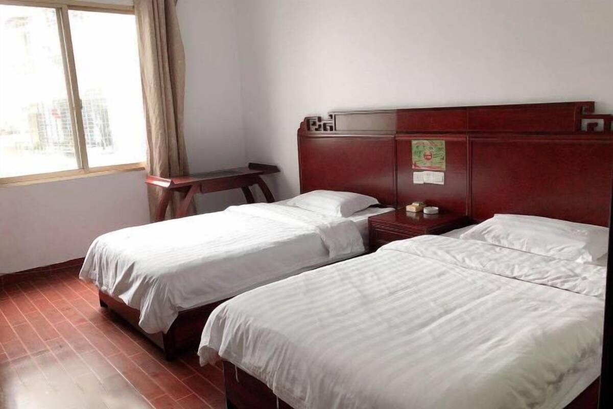 Habitación de hotel con dos camas individuales, una mesita de noche de madera, un escritorio pequeño y una ventana con cortinas.