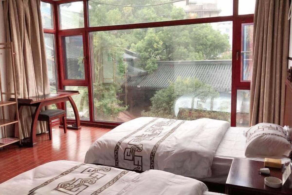 Una habitación con una cama, un escritorio y vistas a un edificio tradicional a través de amplios ventanales.
