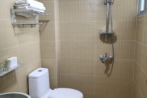 A bathroom with beige tiled walls, a white toilet, a shower with a handheld showerhead, and a towel rack with folded towels. - Shui Jie Hostel (Xing'an County)