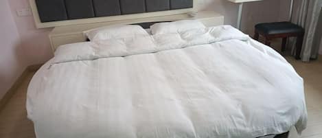 Una cama bien hecha con cabecera, una mesita con una silla y una ventana con cortinas.