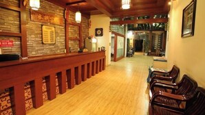 A reception area with a wooden reception desk, a stone wall, and a seating area with chairs. - Shui Jie Hostel (Xing'an County)